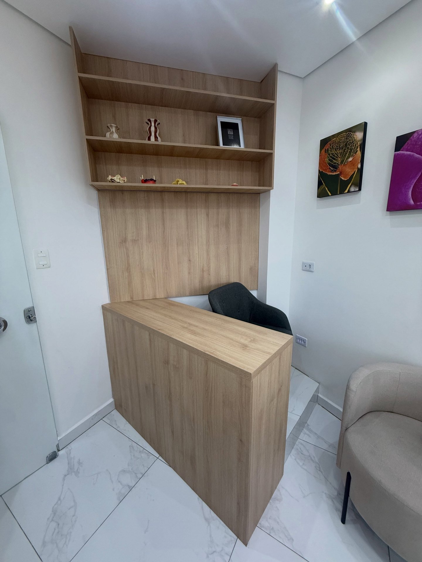 Recepção com balcão em L, painel e estante de prateleiras em madeira clara